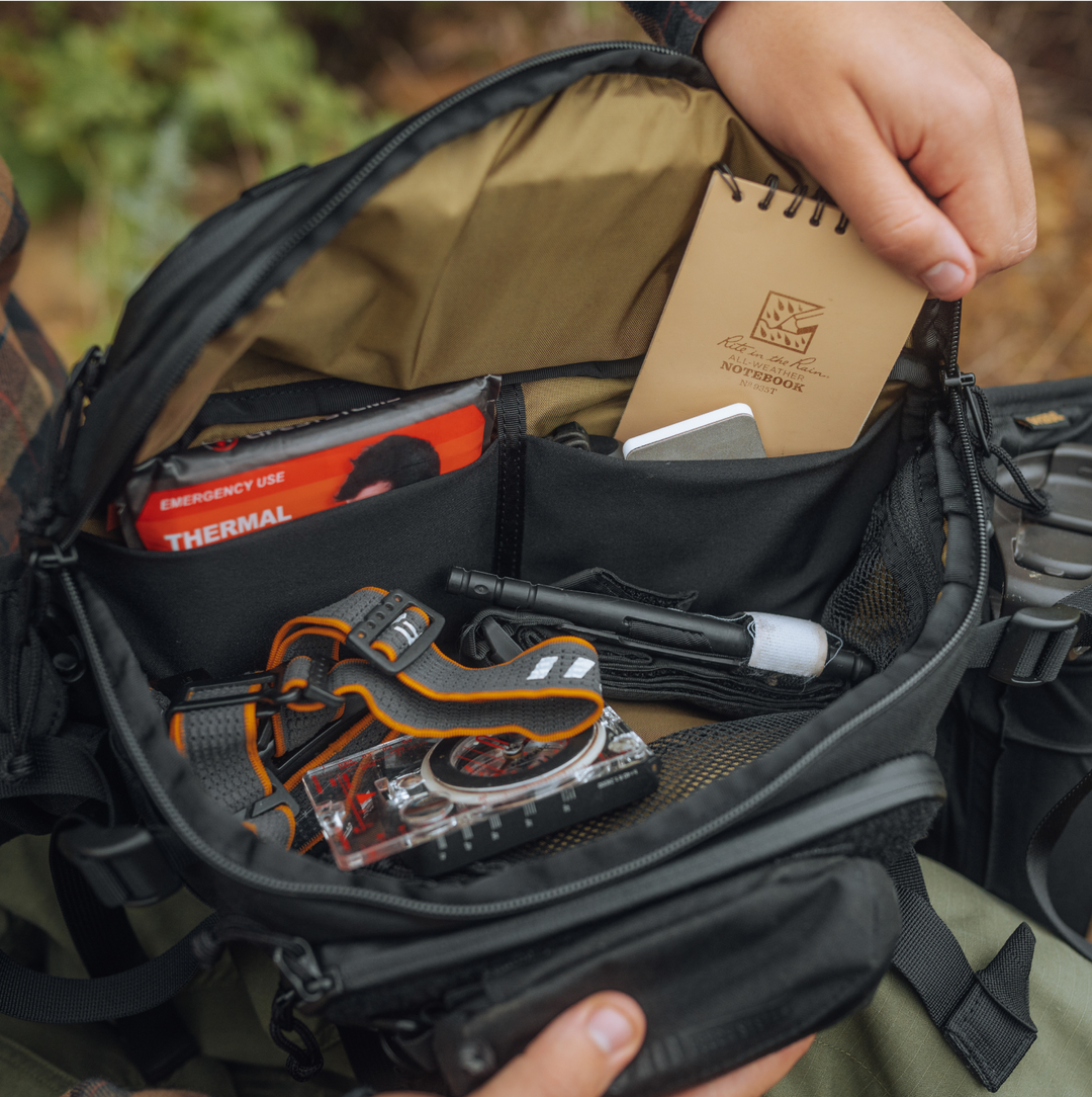 Interior photo of main three panel compartment of 4.5L Mission Hip Pack. Field notes journal, headlamp, compass, emergency first aid kit, pen, light and G-Mod Pod Pouch visible.