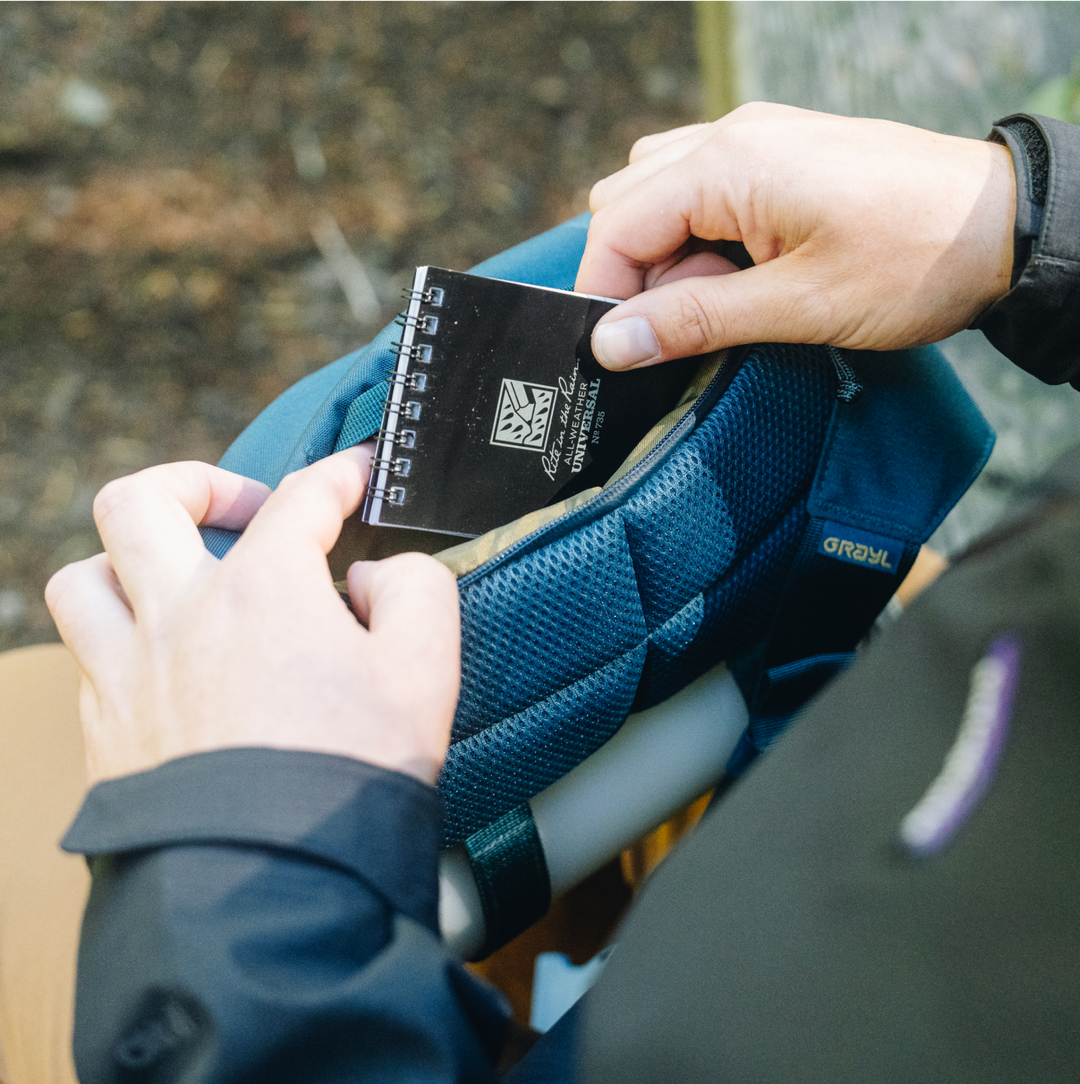 Traveller accessing note pad and passport  in the concealed pocket of a Grayl Transport Hip Pack and Crossbody Sling.