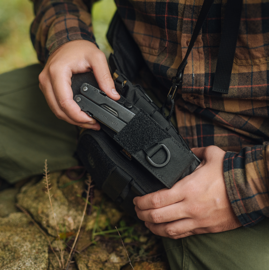 G-MOD Multi-Tool Pouch in Covert Black fastened via molle to Mission Bottle Carrier and Sling. Hiker accessing Leatherman multitool.