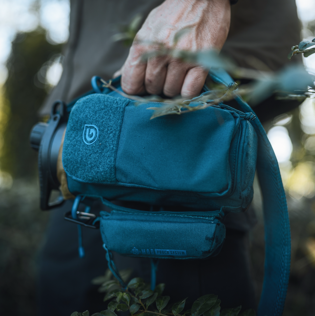 QuickCarry handle being grabbed by hiker while carrying Grayl Transport Bottle Sling in Wander Blue colorway. GeoPress Titanium filter and purifier bottle visible in main compartment.