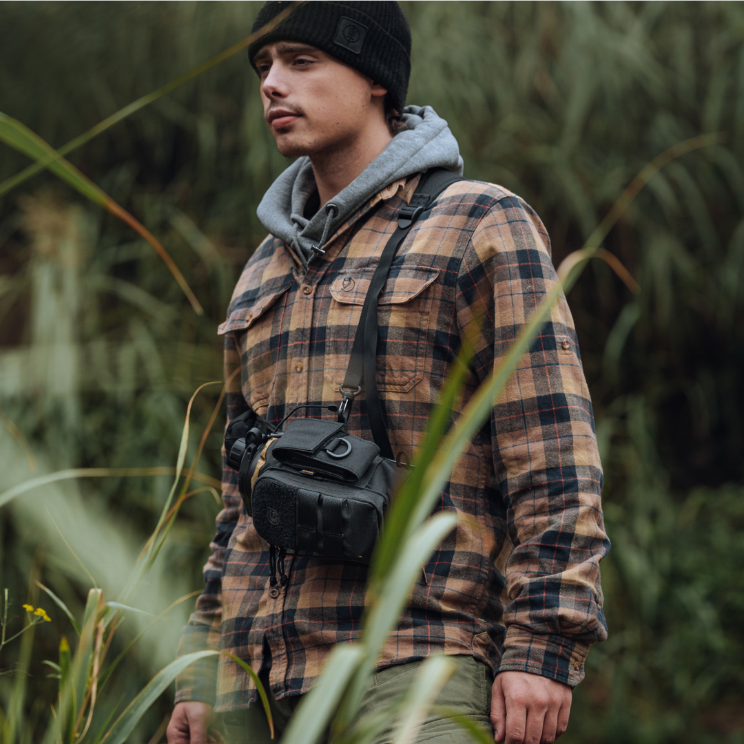 Hiker wearing Grayl® Mission Bottle Sling in Covert Black colorway. Male hiker is Carrying his GeoPress water filter purifier bottle visible in main compartment, strapped across his chest.